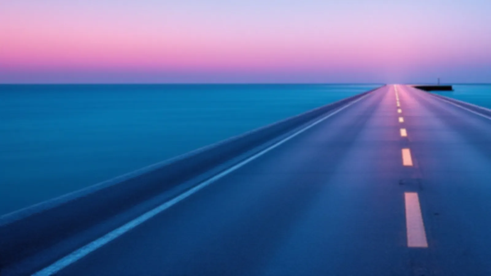 An empty causeway road crossing calm blue water at dawn with soft pink sky, the CoupePay view of payday loans online, $100 – $5,000